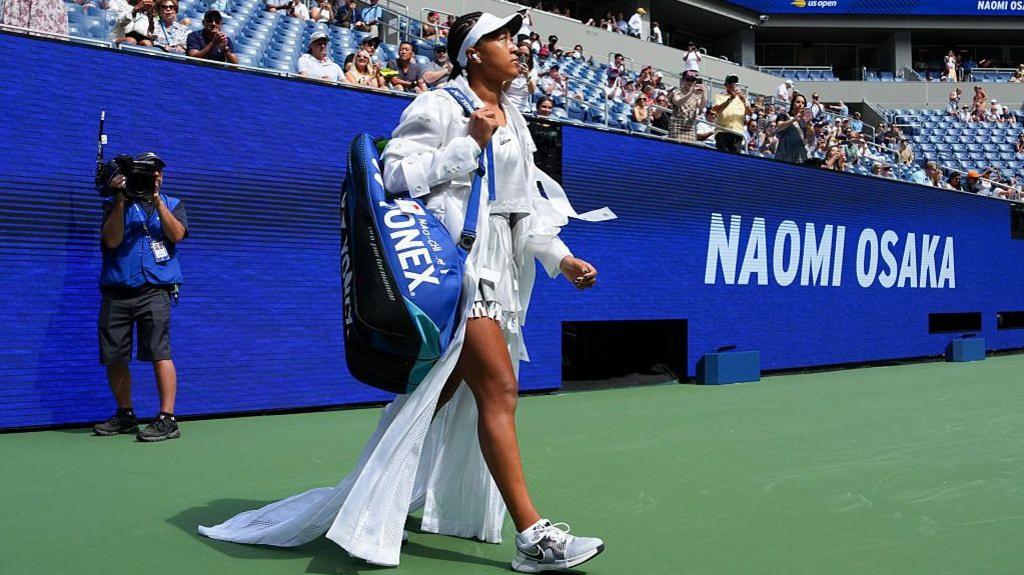 Naomi Osaka walks out on to court wearing a white dress