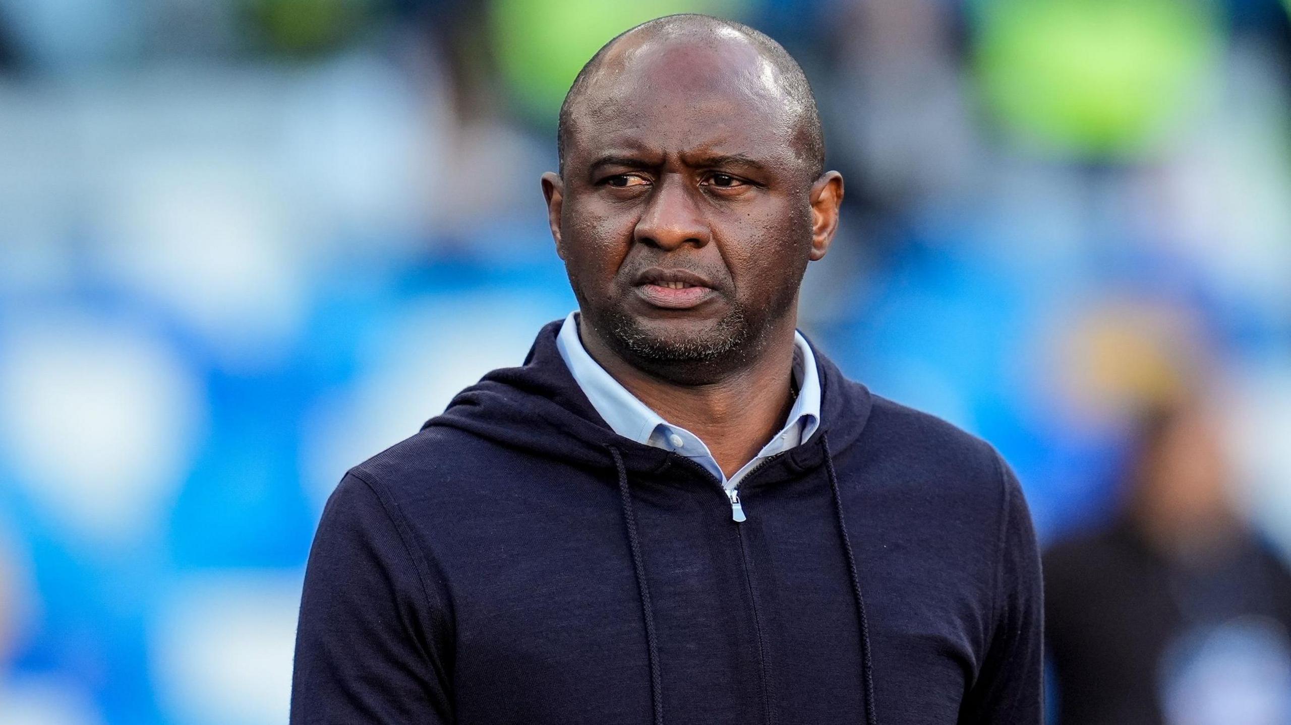 A head and shoulders shot of Patrick Vieira shows him wearing a dark blue hoody over a light blue shirt